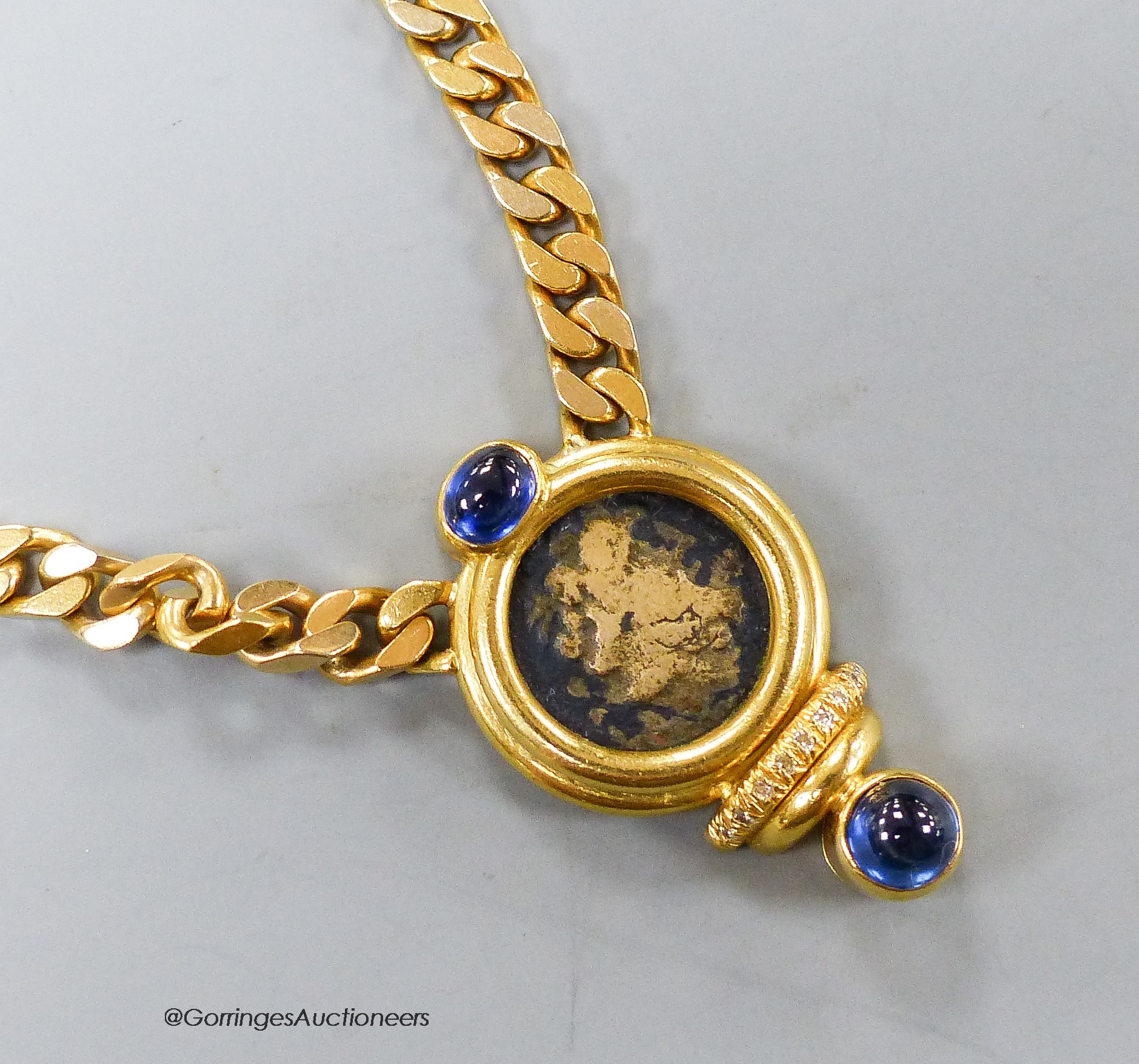 A modern curb link yellow metal, inset coin, blue cabochon stone and diamond set pendant necklace, 43cm, gross weight 47.3 grams.